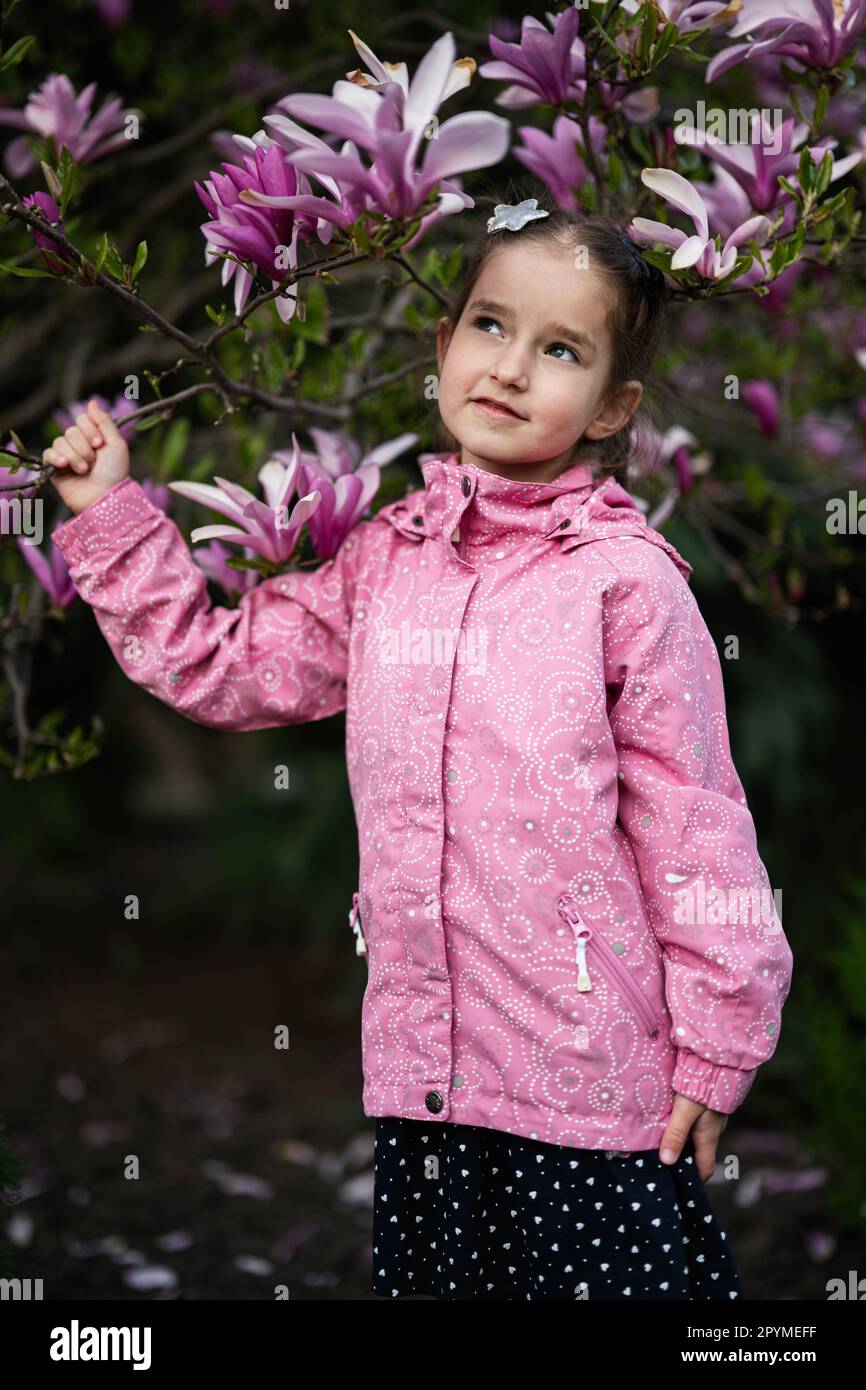 Ragazza preschooler in giacca rosa godendo bella primavera giorno vicino a magnolia albero fioritura. Attività primaverili. Foto Stock