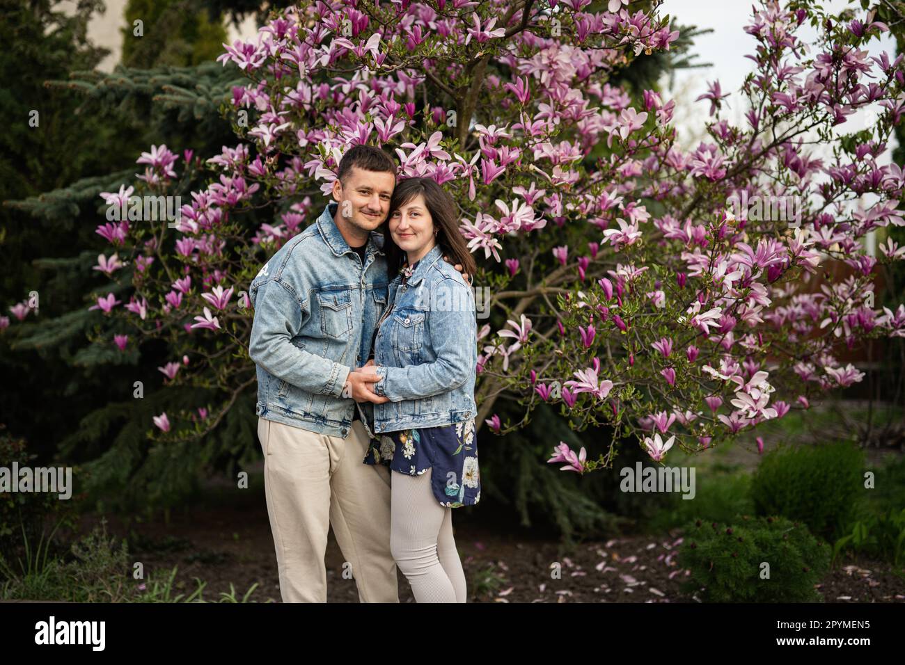 Coppia tenera innamorata indossa una giacca di jeans godendoti una bella giornata primaverile vicino all'albero in fiore di magnolia. Foto Stock