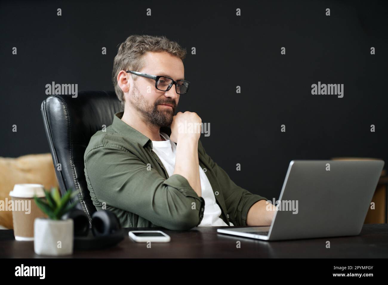 Saggio, uomo caucasico catturato in ritratto, seduto alla scrivania in casa ufficio. Appare premuroso, mentre lavora al computer. Senso di professionalità e produttività in un ambiente di lavoro domestico. Foto di alta qualità Foto Stock