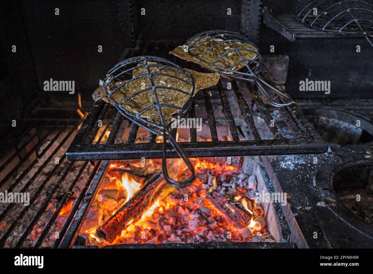 Cucinare il pesce in gabbie di ferro sopra fuoco di legno al ristorante Brat a Londra, Regno Unito Foto Stock