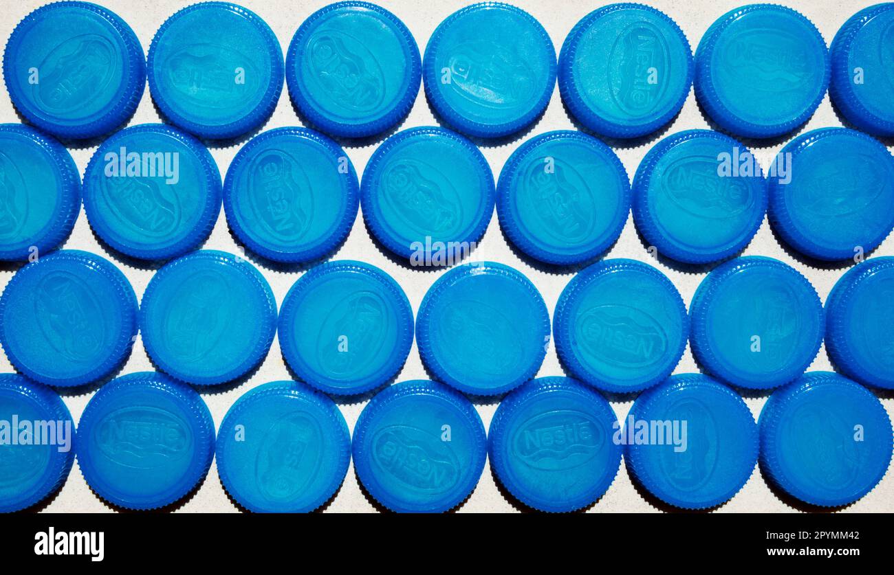Molti tappi di plastica blu per bottiglie con logo Nestle disposti in file su fondo piatto. Nome della società su un gruppo di acqua potabile la vie tappi preparati fo Foto Stock