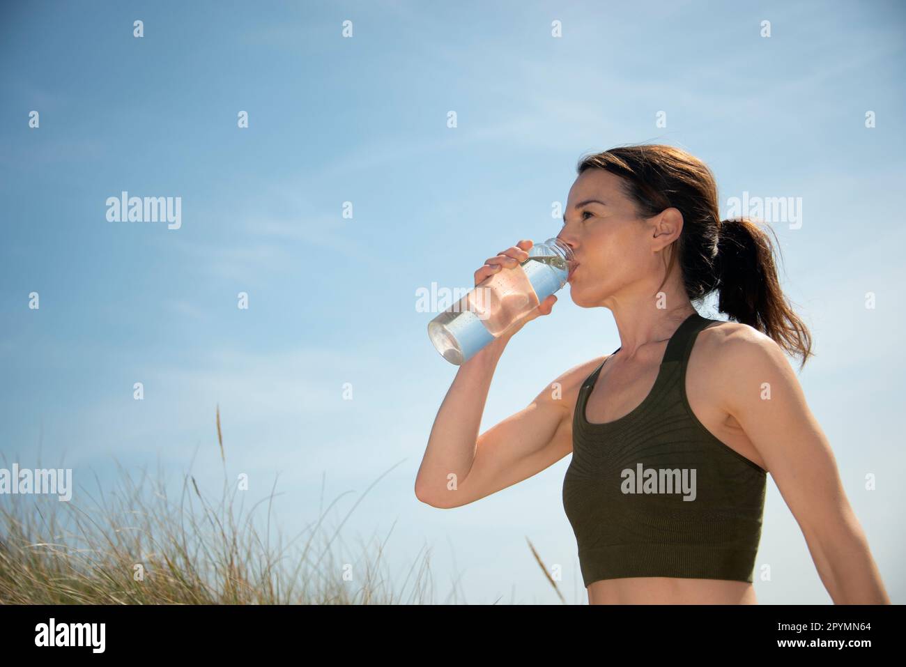 Donna sportiva e in forma che beve acqua da una bottiglia d'acqua di vetro dopo l'esercizio fisico e la corsa all'aperto. Foto Stock