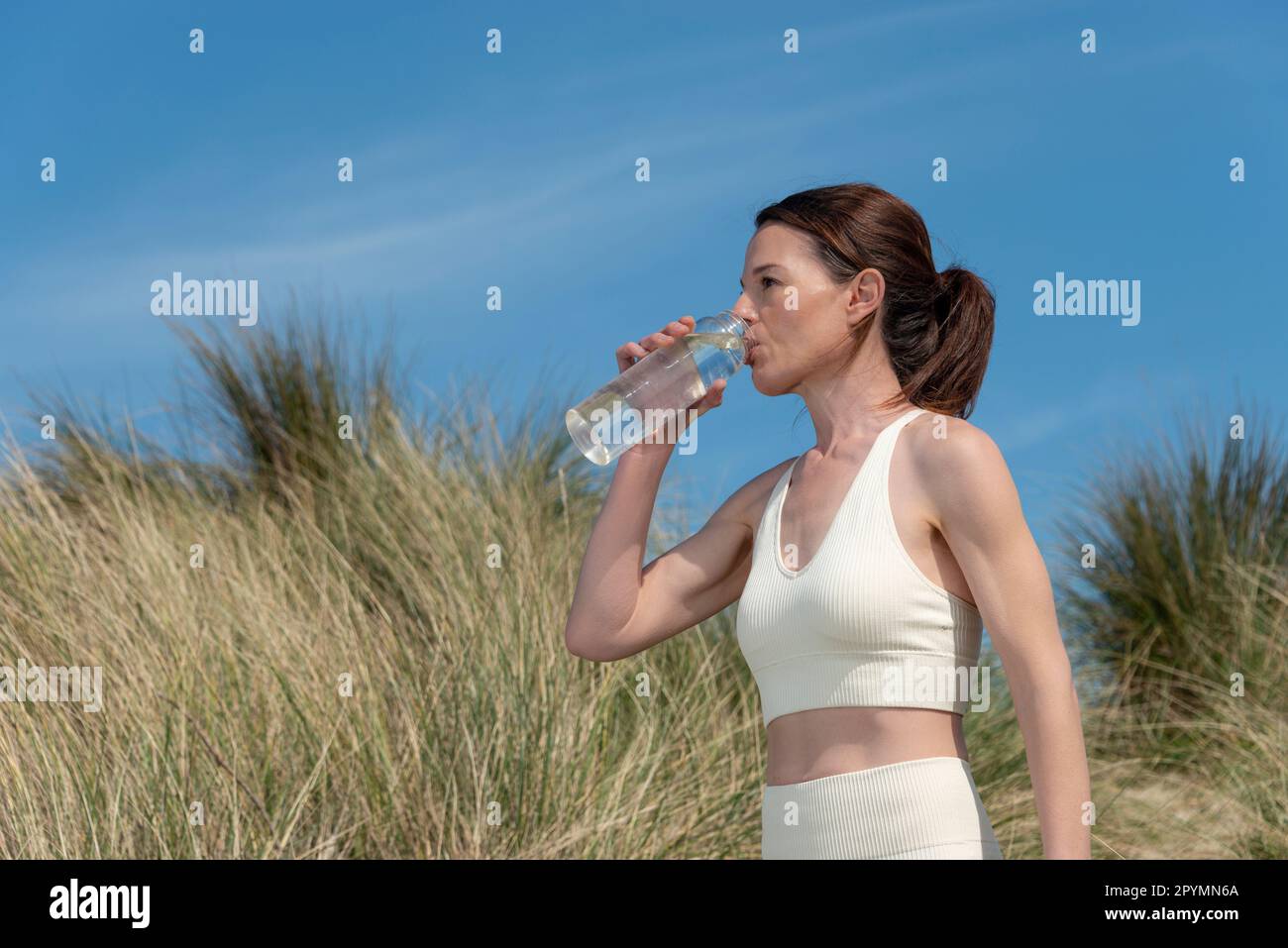 Donna adulta media sportiva che prende una bevanda d'acqua da una bottiglia di vetro dopo l'esercizio fisico. Foto Stock