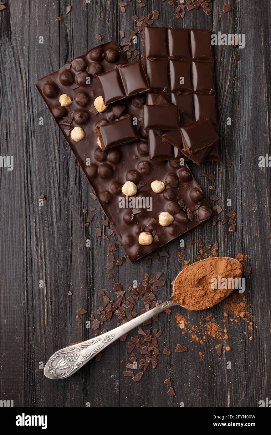 Cioccolato fatto a mano con nocciole, pezzi di cioccolato fondente, cacao in un cucchiaio d'annata su uno sfondo di legno scuro vista dall'alto. Concetto di varietà di cioccolato. Foto Stock