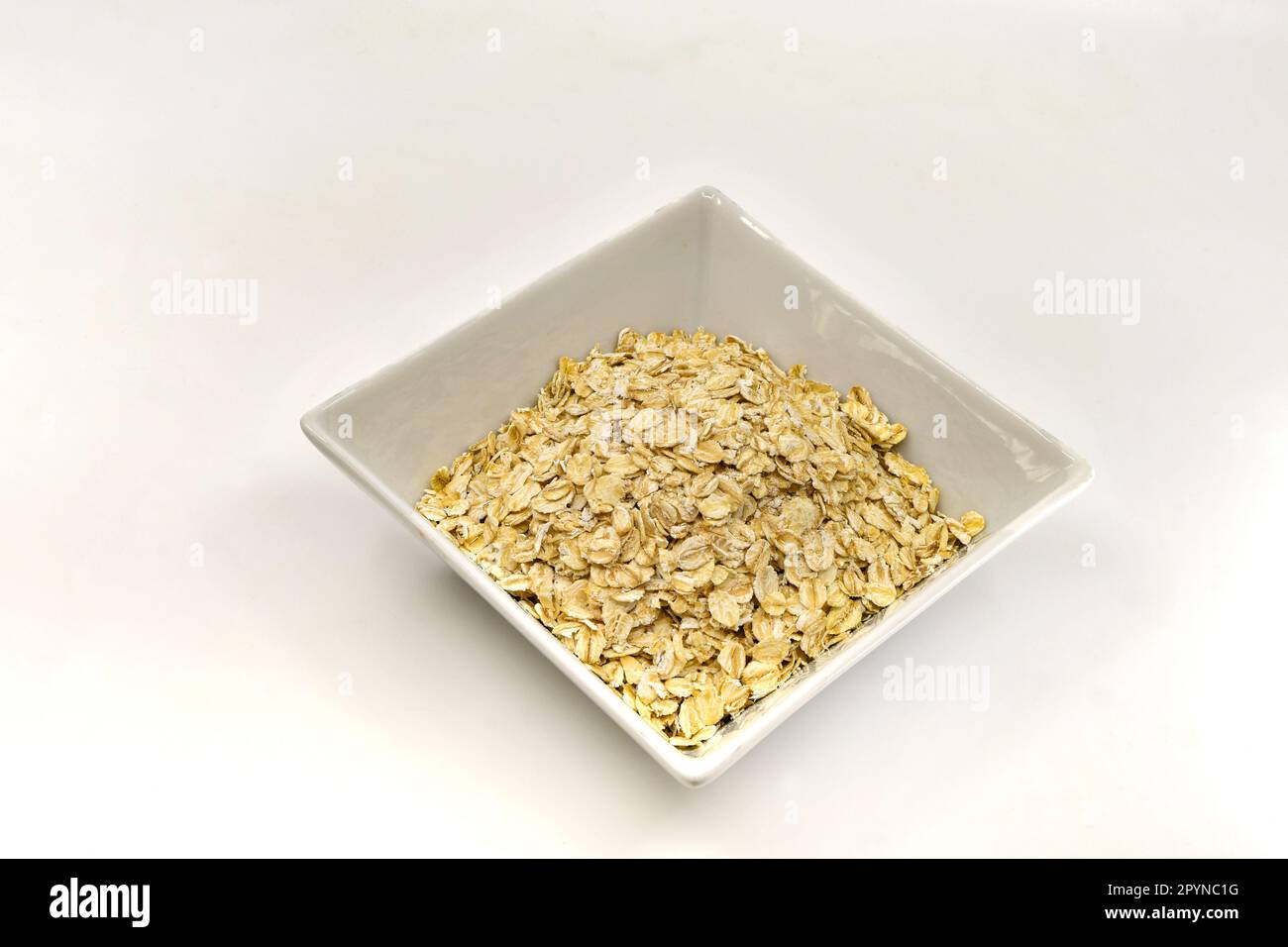 Avena in una ciotola quadrata isolata su fondo bianco. Spazio di copia. Nessuna gente. Foto Stock