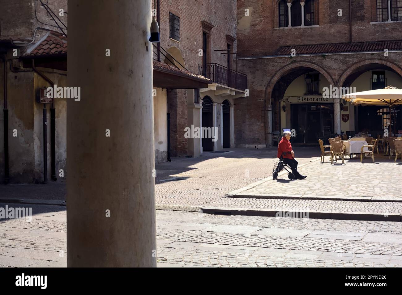 Vecchia donna seduta da sola su un camminatore in una piazza vuota sotto il  sole Foto stock - Alamy