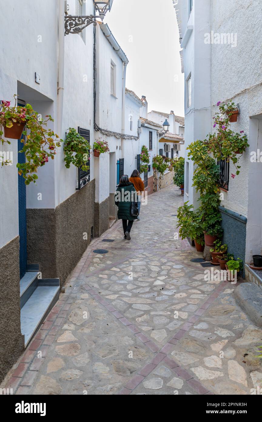 Due donne viste da dietro camminando attraverso una strada pedonale stretta tipica di Castril, Granada (Spagna) con vasi di fiori sui lati Foto Stock