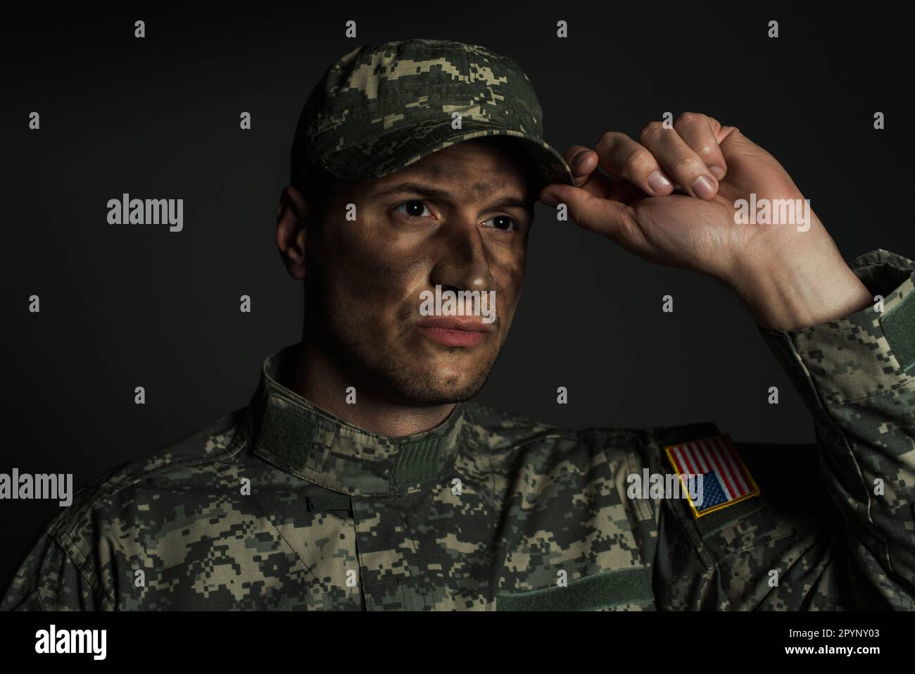 uomo militare con sporco sul viso in piedi in uniforme e cappuccio di regolazione isolato su grigio, immagine stock Foto Stock