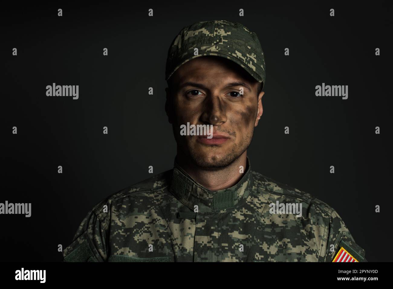 uomo militare con sporco sul viso in piedi in uniforme e cappuccio isolato su grigio, immagine stock Foto Stock