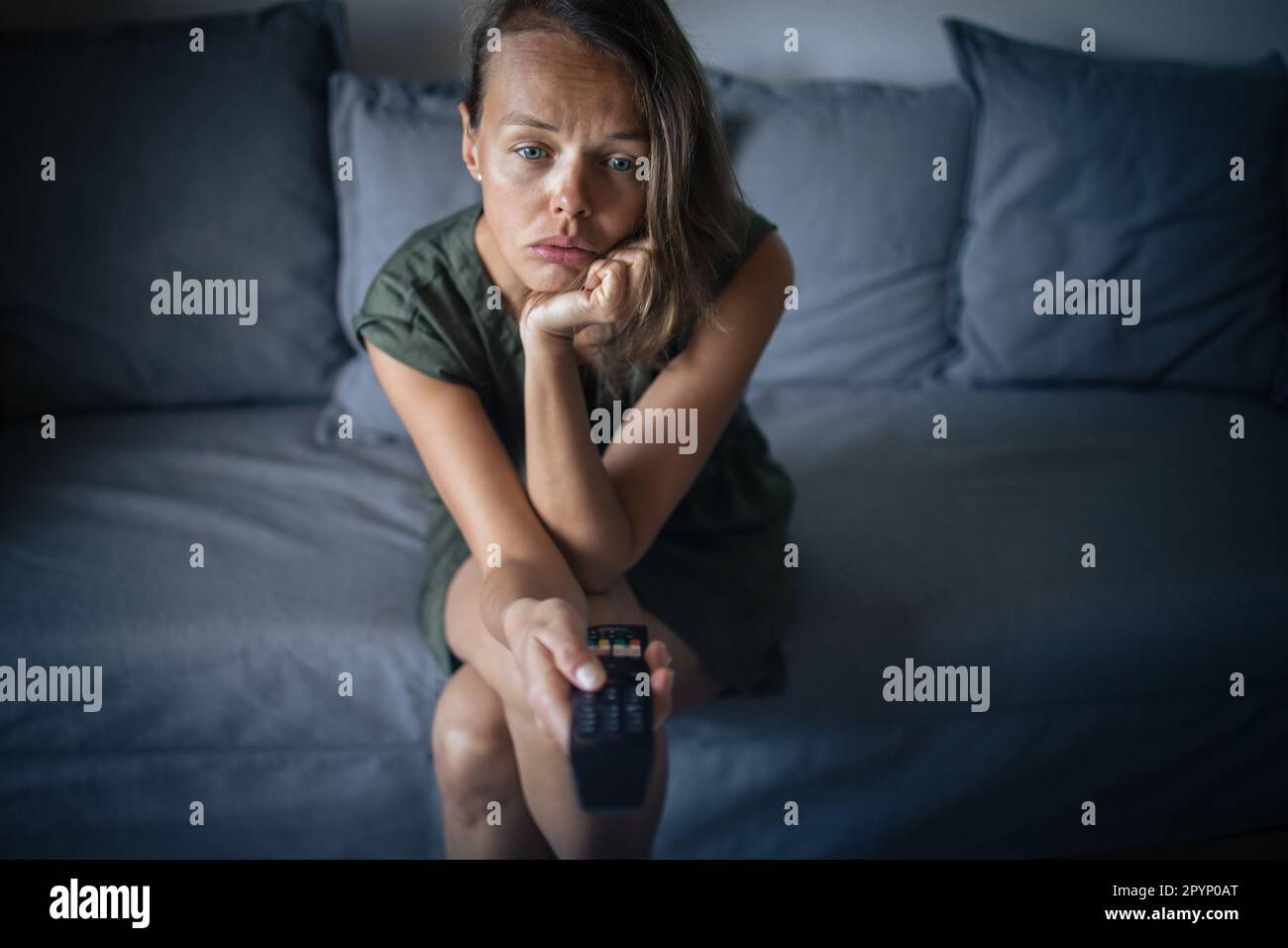 Bella, giovane donna seduta sul divano al coperto a casa e guardare la TV Foto Stock