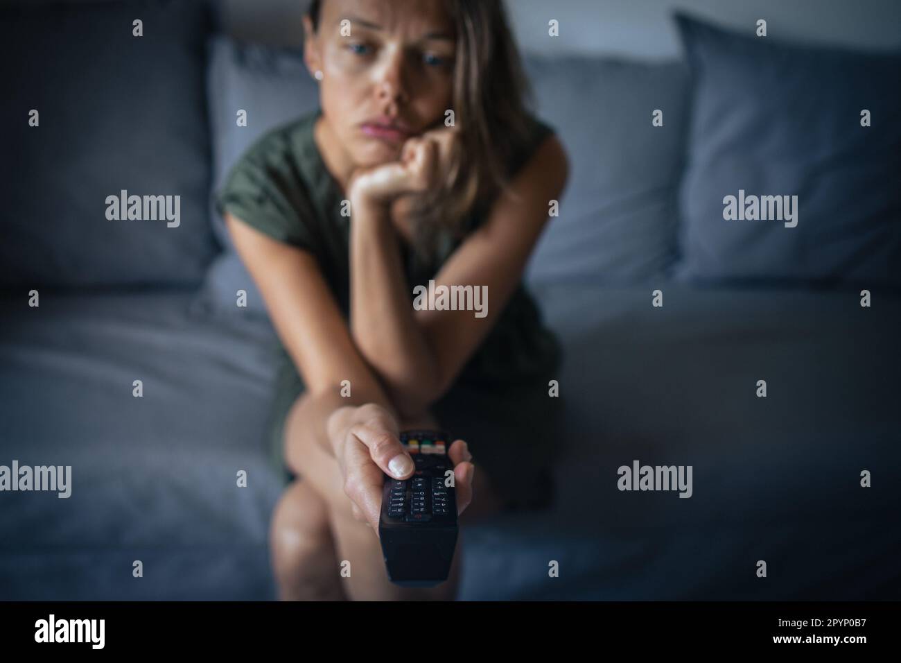 Bella, giovane donna seduta sul divano al coperto a casa e guardare la TV Foto Stock