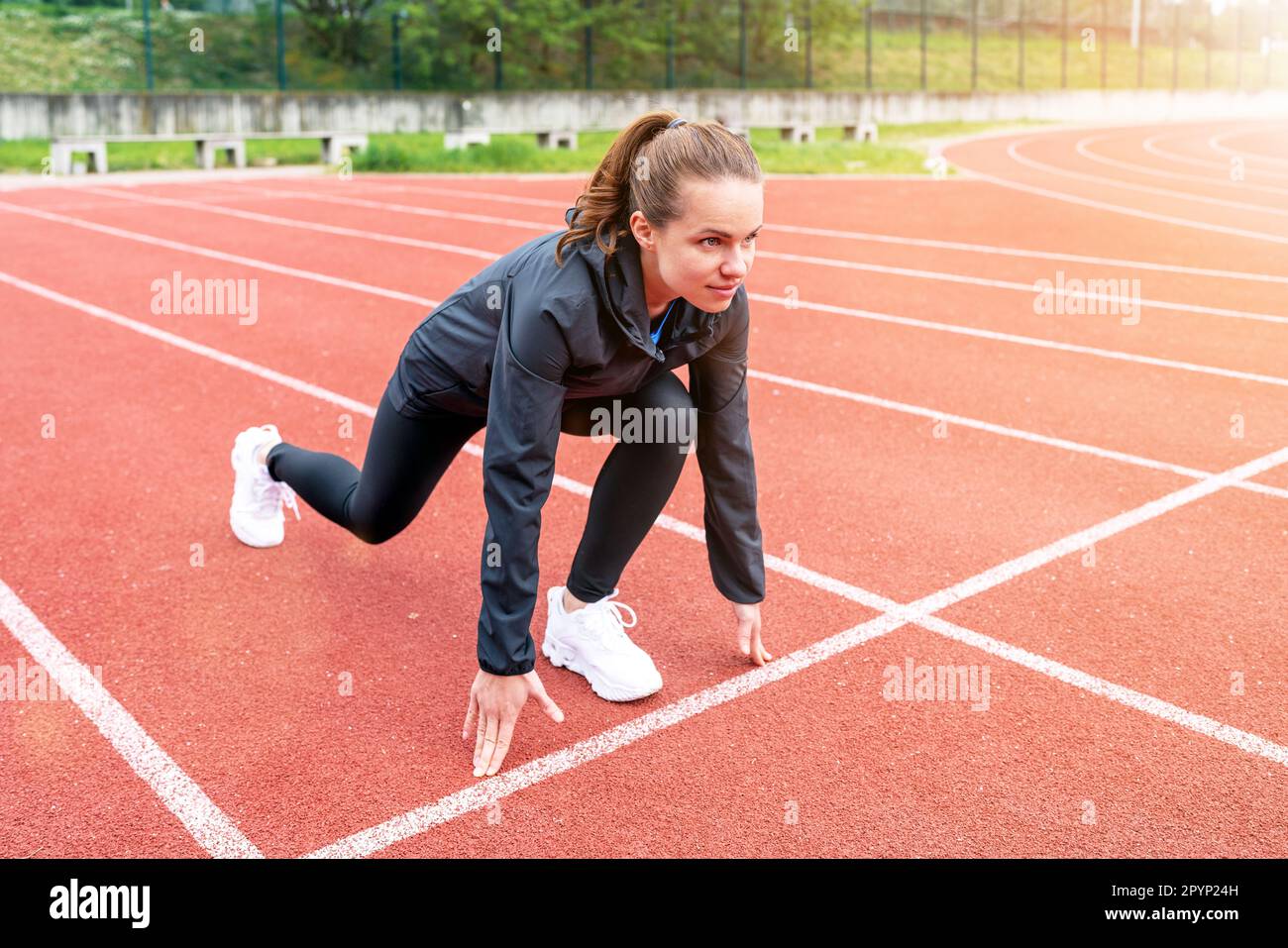 Bruna donna runner in posizione di partenza sulla pista di corsa durante l'allenamento. Foto Stock