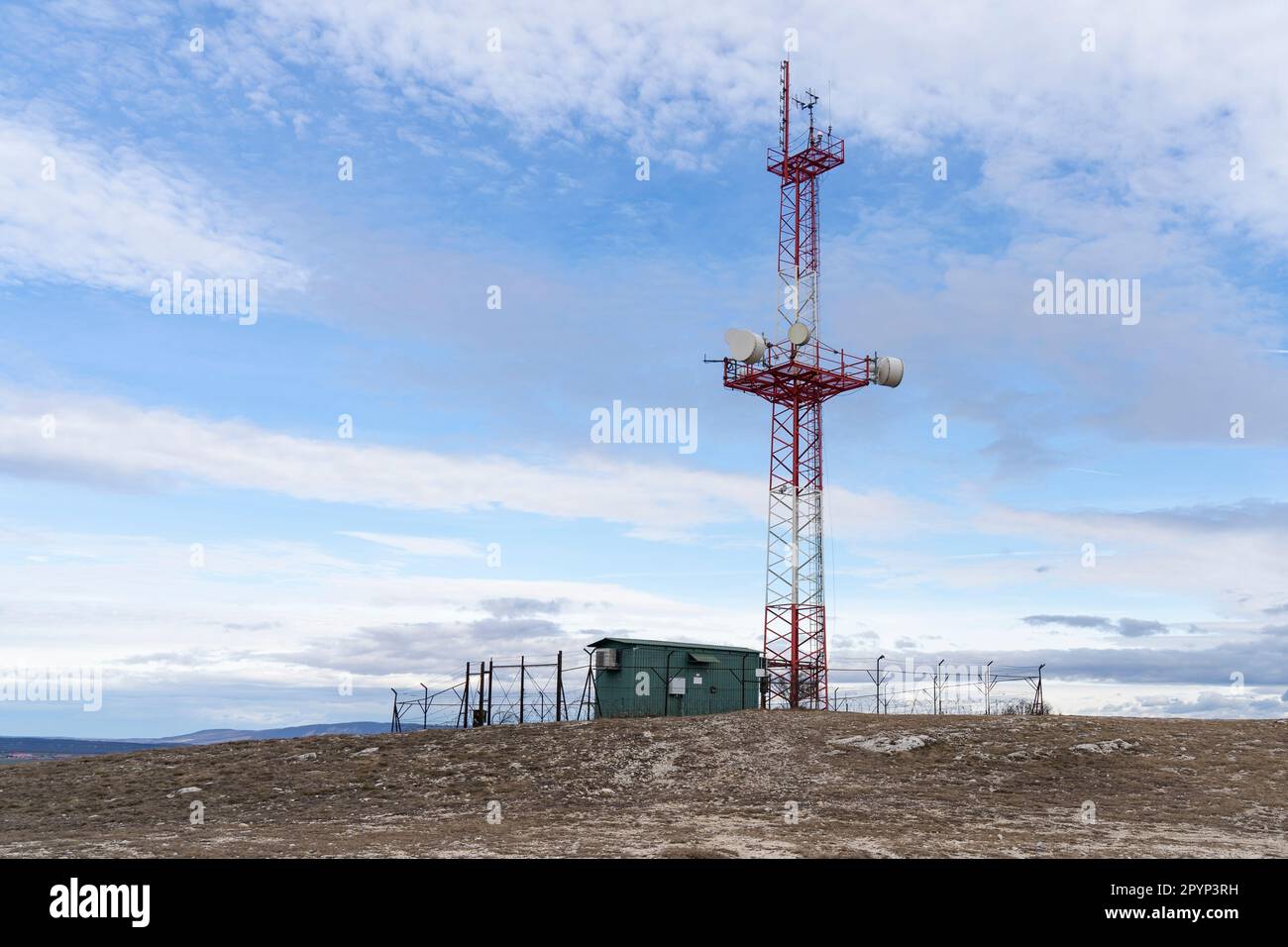 Torre di comunicazione con annesso verde e recinzione metallica con cielo blu sullo sfondo Foto Stock