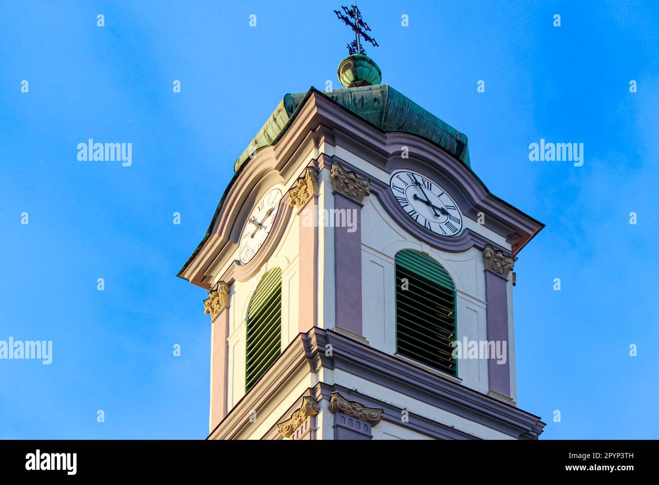 Torre barocca bianca e viola con tetto e croce ricoperta di patina verde, orologio torre e doghe verdi Foto Stock