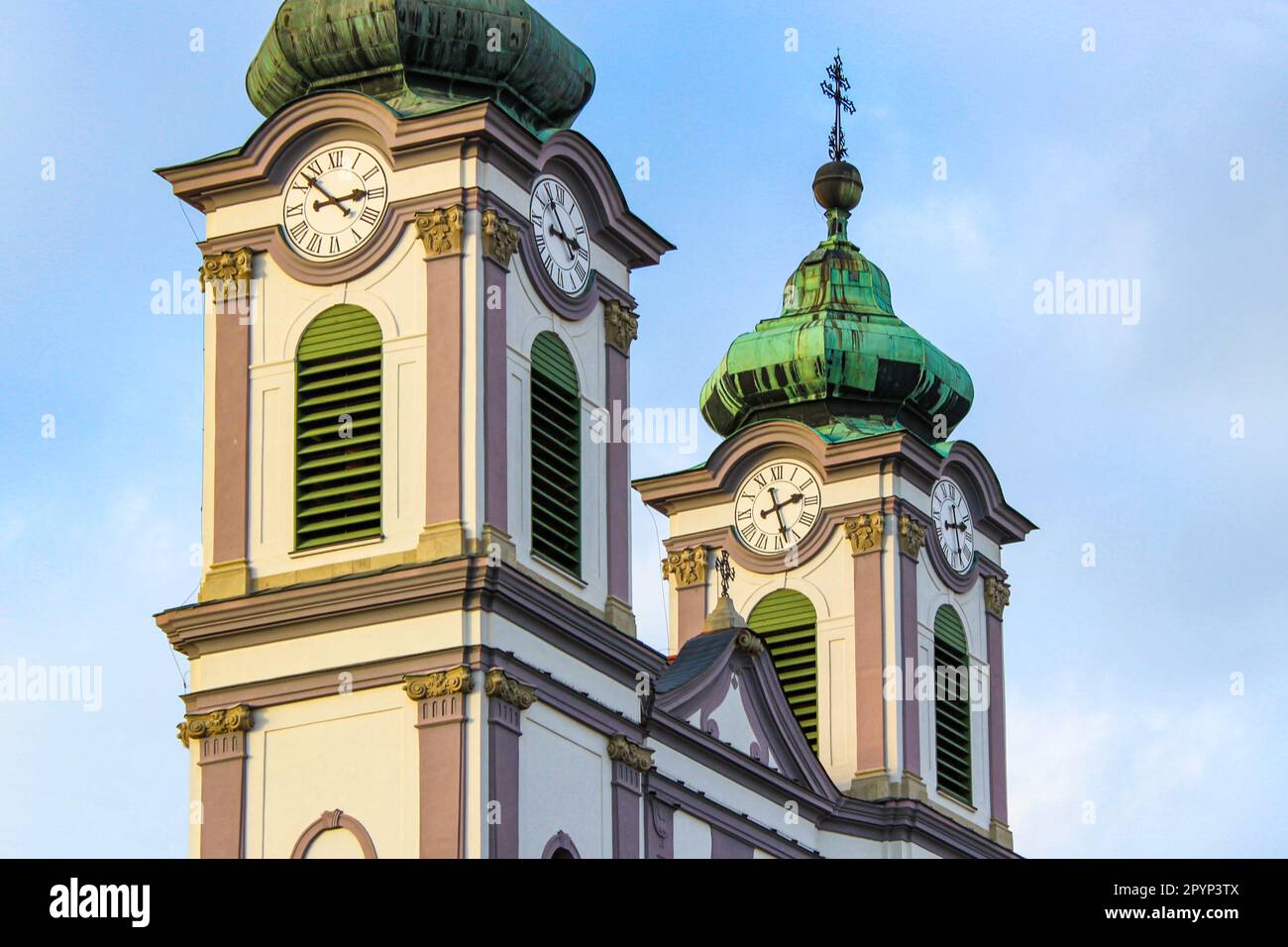 Torri barocche bianche e viola con tetto e croce ricoperta di patina verde, orologio a torre e doghe verdi Foto Stock