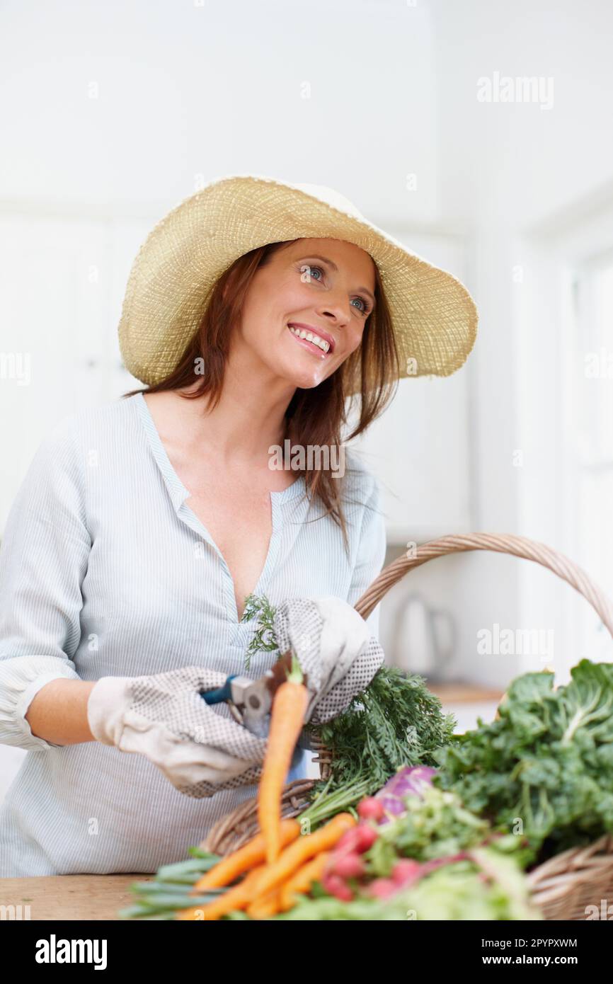 La vita semplice. Una donna splendida, che indossa un cappello di paglia,  taglia i gambi di verdure fresche in un cestino sul bancone della cucina  Foto stock - Alamy