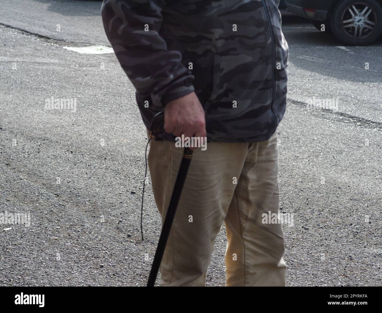 Macrofone di un uomo anziano irriconoscibile che tiene il manico di legno di una canna da passeggio, all'aperto per strada Foto Stock