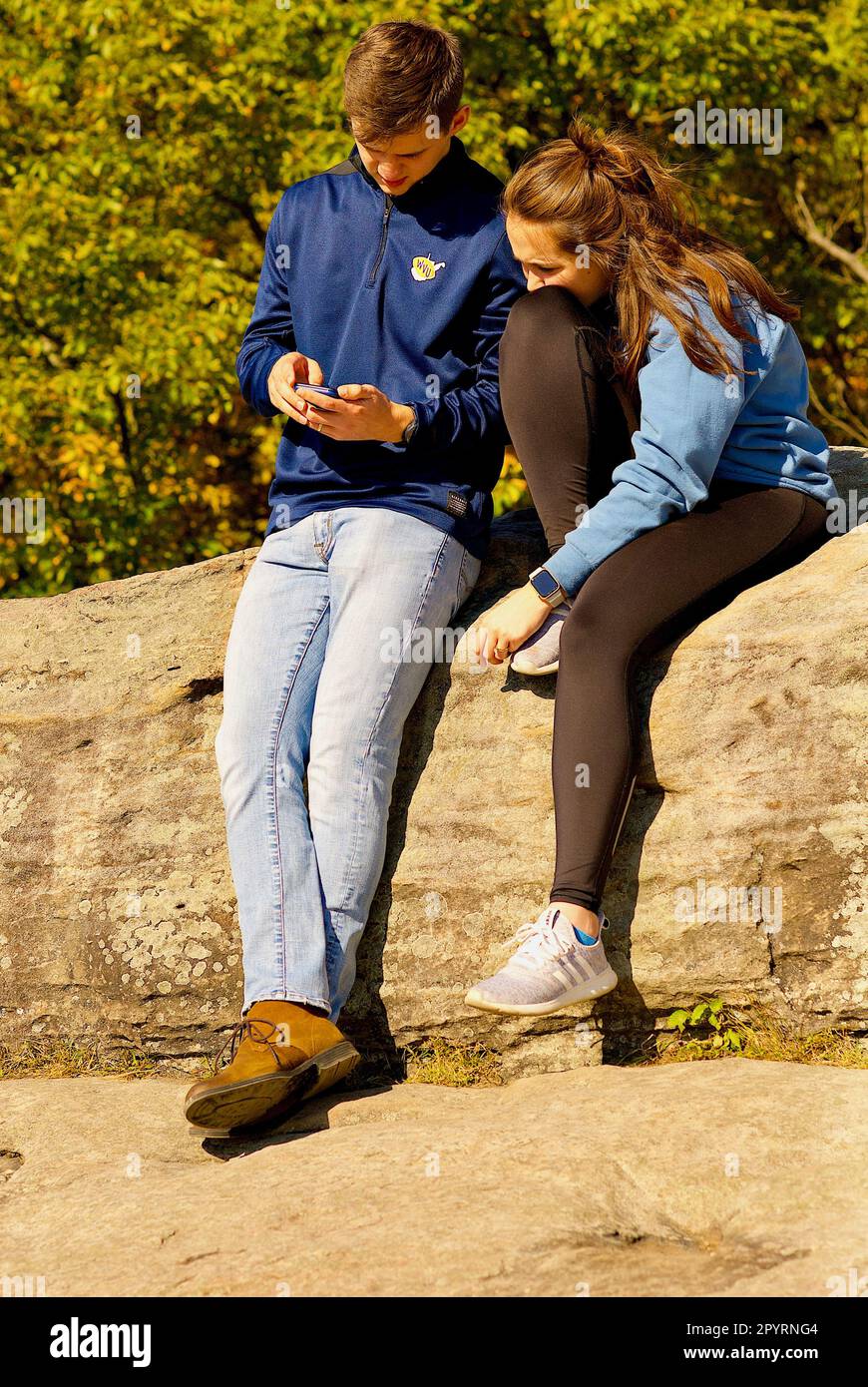 Una giovane coppia sposata guarda uno smartphone mentre si gode l'aria aperta alla Coopers Rock state Forest nella Virginia Occidentale in un pomeriggio di sole autunnale. Foto Stock