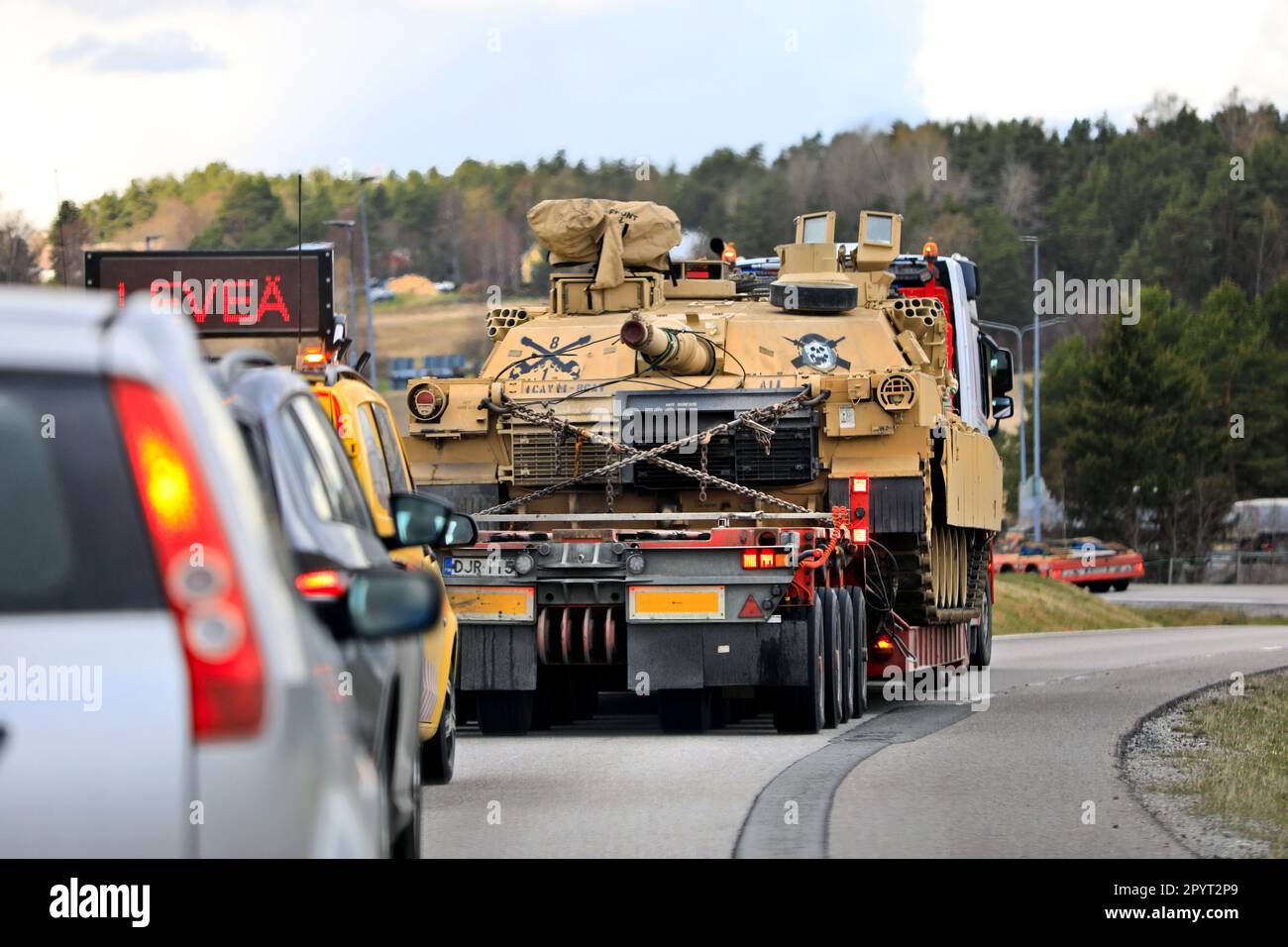 Camion trasporti American M1 Abrams carro armato militare su rimorchio a bassa caricatrice su rampa autostradale assistita da veicolo di scorta. Salo, Finlandia. Aprile 28, 2023. Foto Stock