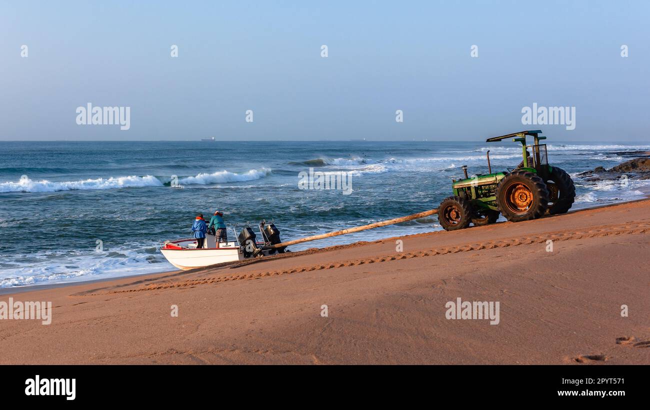 Barca da pesca entrata in surf onde oceaniche al largo della spiaggia di sabbia da trattore utilizzando legno palo metodo di spinta in acque marine all'alba . Foto Stock