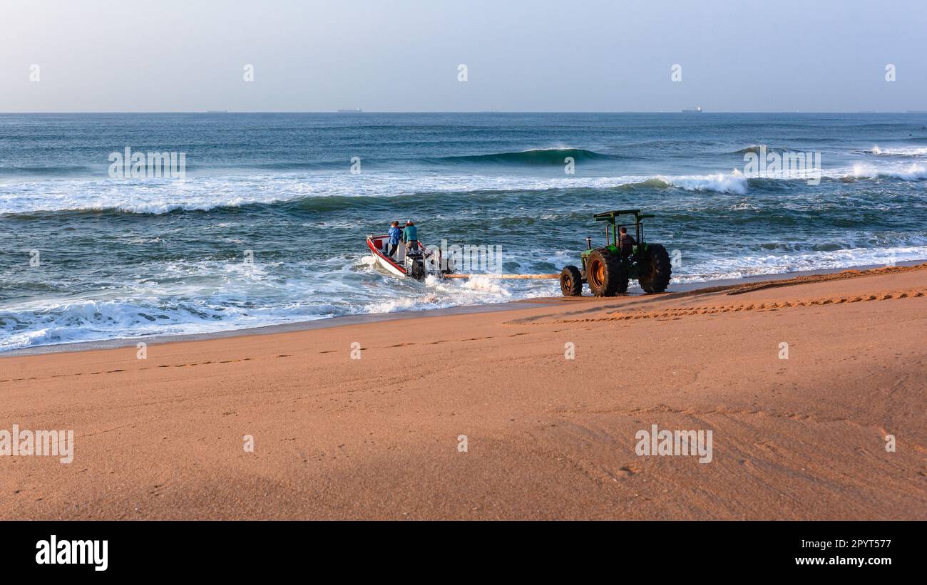 Barca da pesca entrata in surf onde oceaniche al largo della spiaggia di sabbia da trattore utilizzando legno palo metodo di spinta in acque marine all'alba . Foto Stock