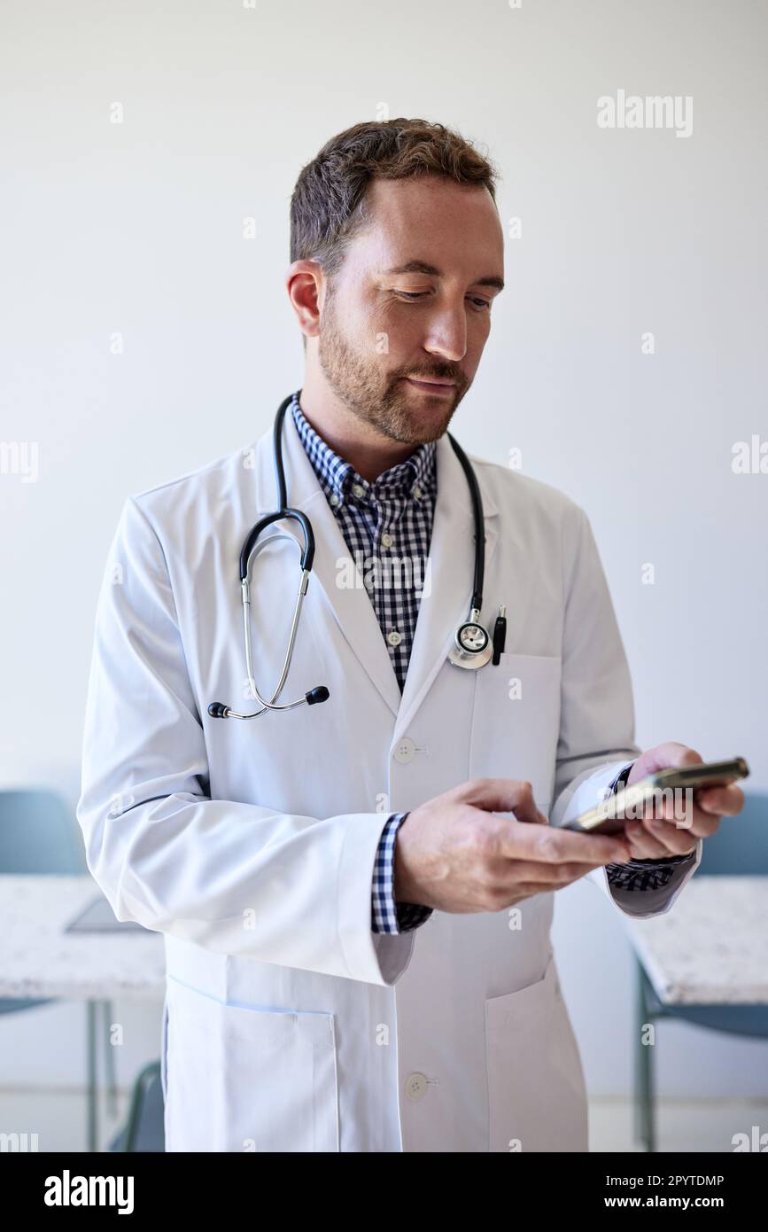 Medico maschile navigare in rete attraverso smartphone mentre si è in piedi in clinica Foto Stock