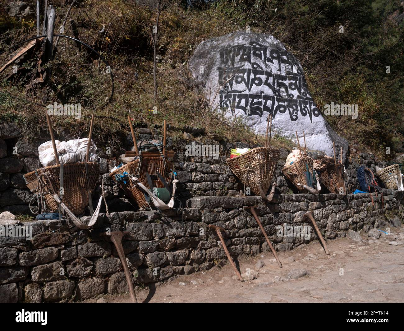 Cestini portieri pieni di cibo e bevande e bastoni da passeggio con il mantra buddista 'Om Mane Padme Hum' scolpito su una roccia sullo sfondo. Everest Bas Foto Stock