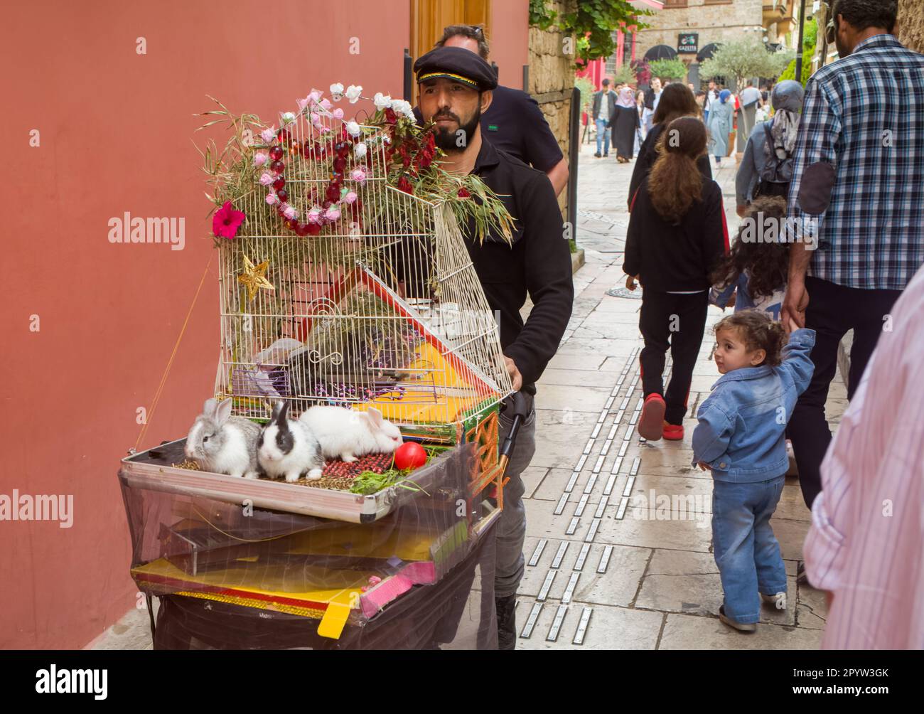 Un uomo spinge un prramma decorato che porta una gabbia e tre conigli bambino come un bambino orologi nella città vecchia di Kaleici, Antalya, provincia di Antalya, Turchia (Turkiy Foto Stock