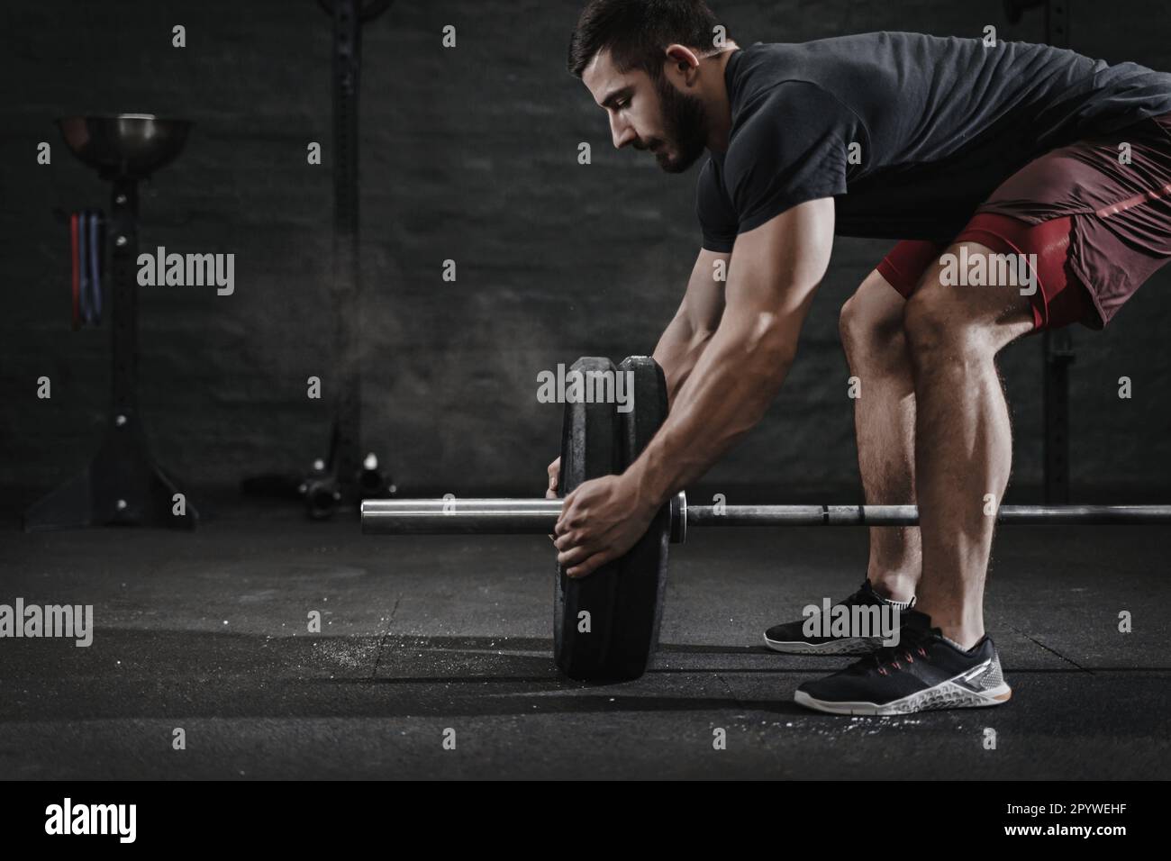 Giovane atleta di crossfit che prepara il barbell per sollevare il peso in palestra. Nuvola di polvere di protezione da magnesia. Bell'uomo che fa allenamento funzionale. Pratica del powerlifting. Esercizi di allenamento. Foto Stock