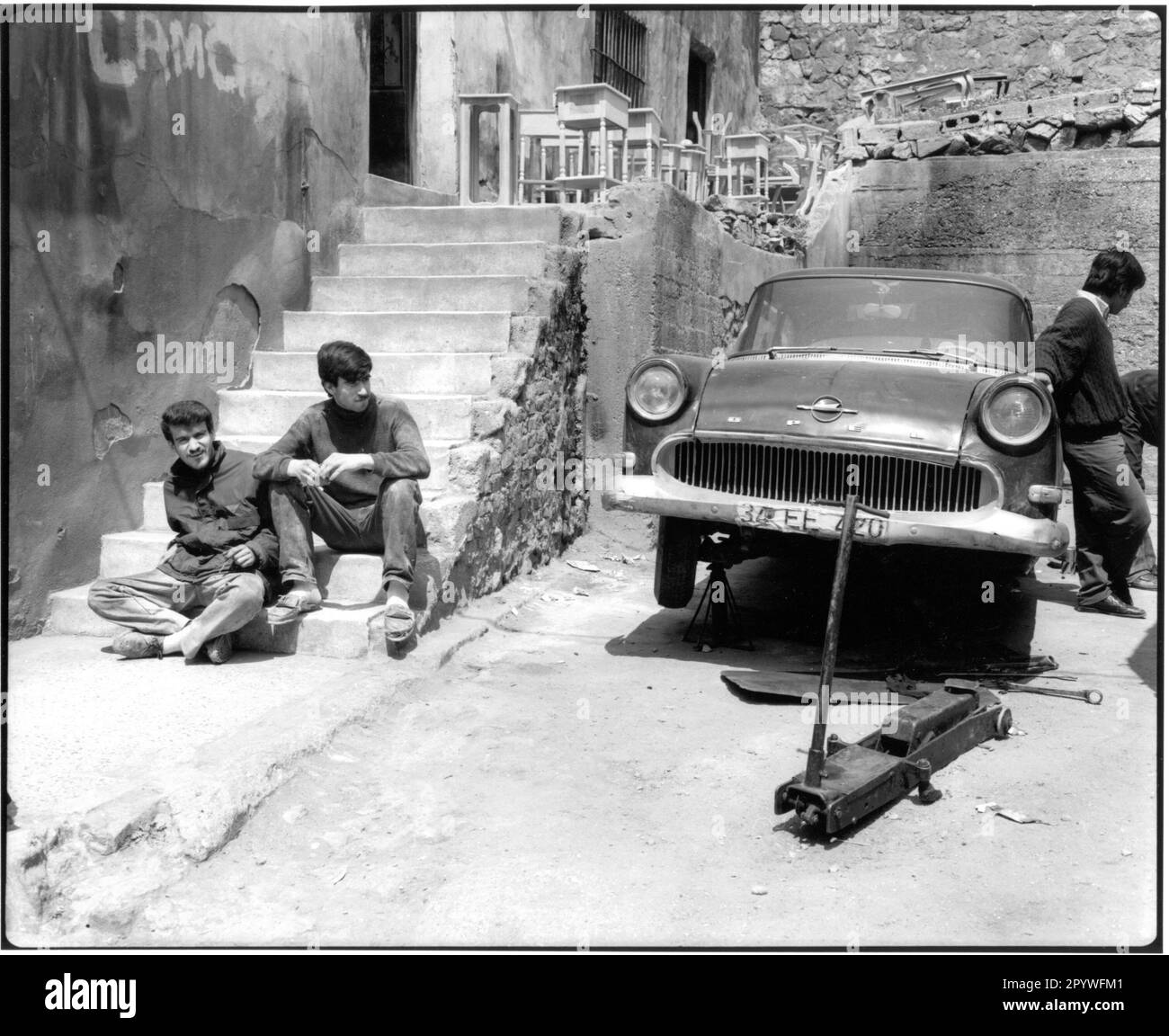 Istanbul (Turchia). Street scene: Uomini durante la pausa pranzo (quartiere Beyoglu) accanto a un vecchio, saccheggiato Opel, auto in riparazione. Bianco e nero. Foto, 1994. Foto Stock