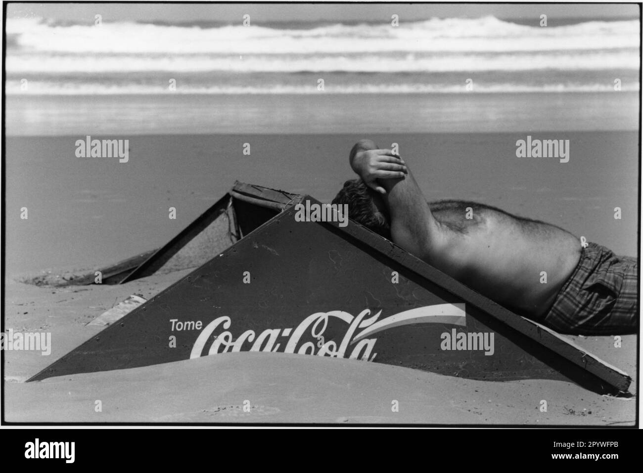 Uruguay, Punta del Este. Solarium. Viaggio e tempo libero: Un uomo si appoggia a un tabellone di Coca-Cola sulla spiaggia, con le onde dell'Atlantico sullo sfondo. Beach scene, in bianco e nero. Foto, 1997. Foto Stock