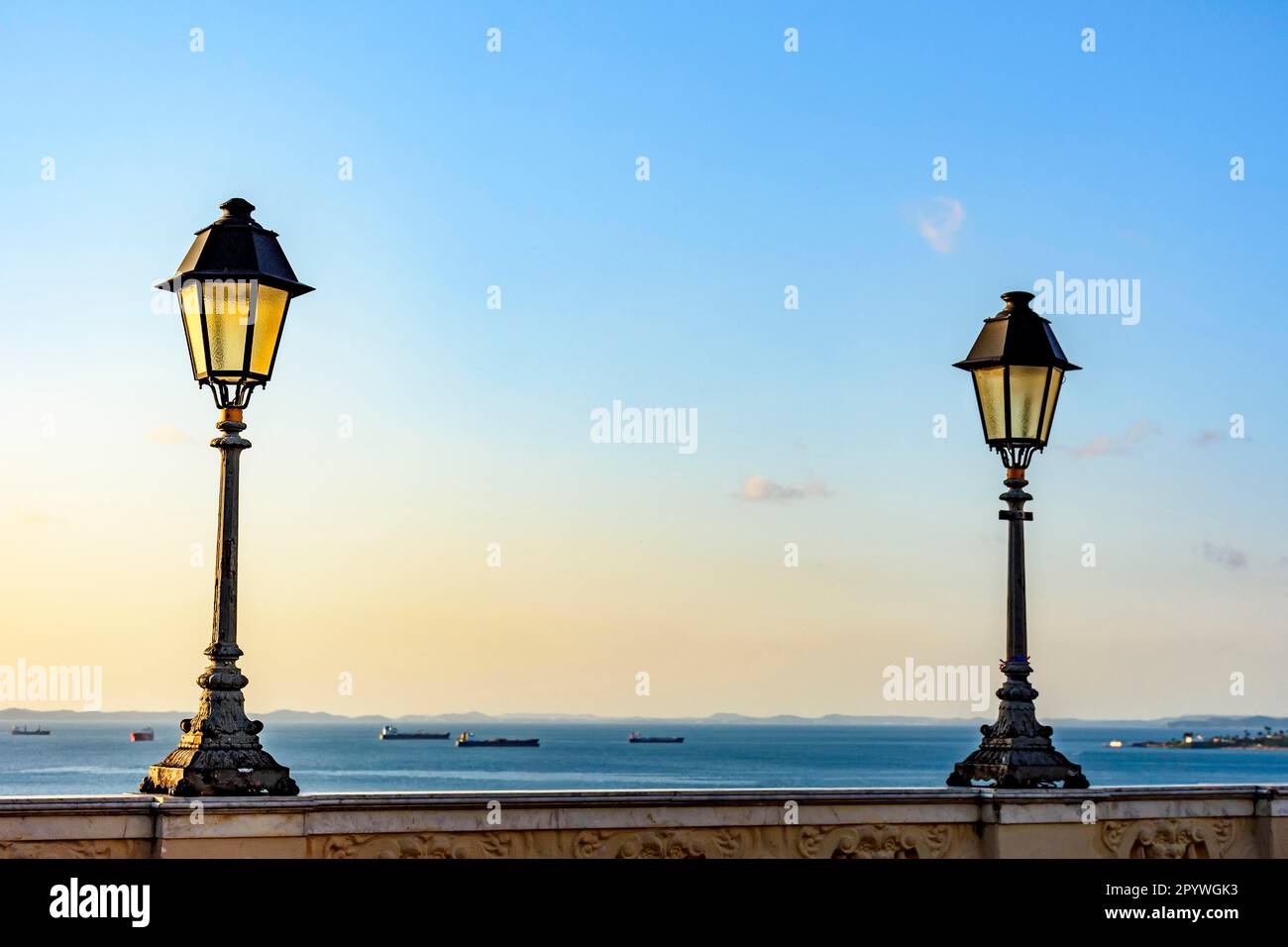 Vecchie lanterne illuminano le pareti nelle strade di Salvador con la baia di tutti i Santi sullo sfondo con le loro barche durante il tramonto, Brasile Foto Stock