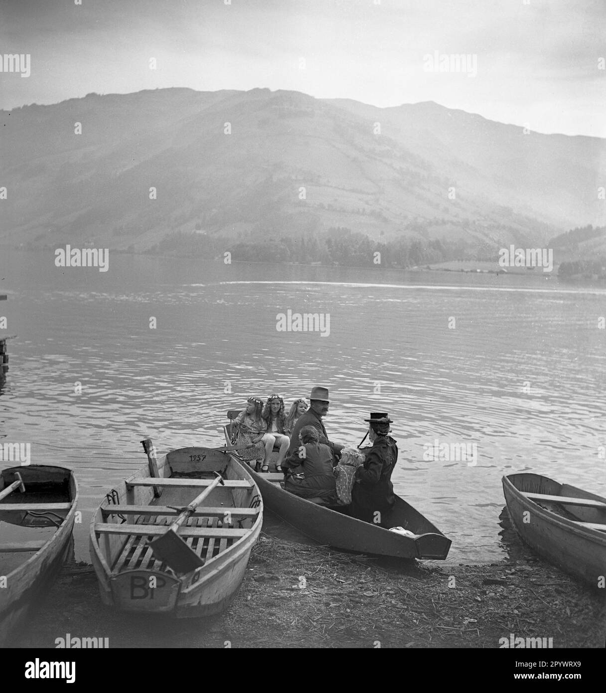 Persone in barca sulla riva del Lago di Zell. Sullo sfondo un caffè e un posto barca ormeggio. La famiglia è sulla strada per un St. Festa di Maria a Zell. Foto Stock