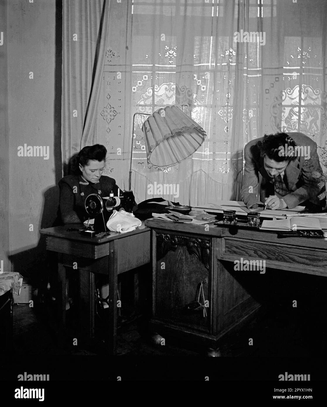 "Una donna lavora su una macchina da cucire. L'uomo nella foto è occupato di disegni tecnici. Scena della serie ''We Work Together''. Il fotografo accompagna le coppie nelle loro rispettive occupazioni." Foto Stock