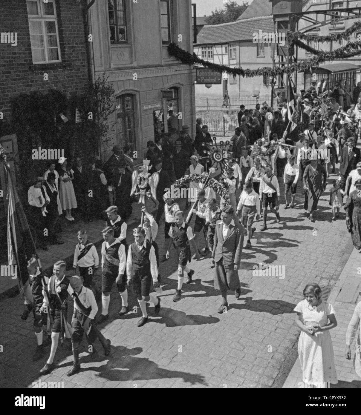 Nell'ambito del festival dei bambini, i bambini sfilano per le strade della città di Plau, Meclemburgo. Portano corone floreali e bandiere. All'estrema destra c'è anche una bandiera della svastika (sparo non datato). Foto Stock