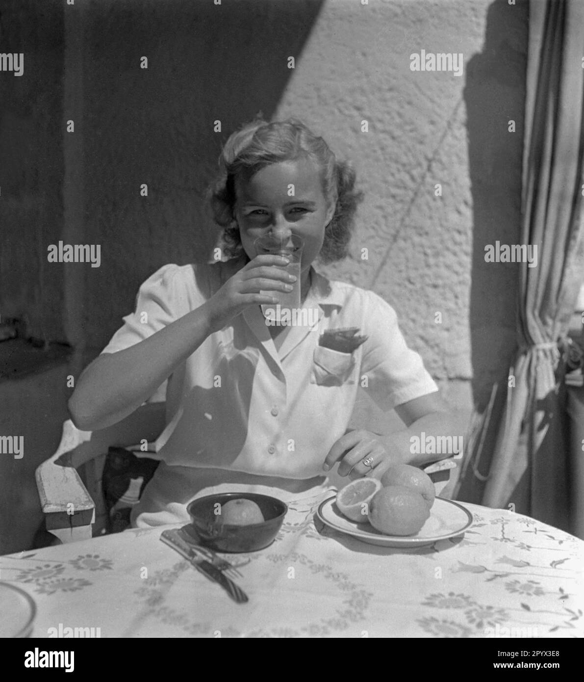 Una donna beve un bicchiere di succo d'arancia appena spremuto. Davanti a lei c'è una centrifuga. Foto Stock