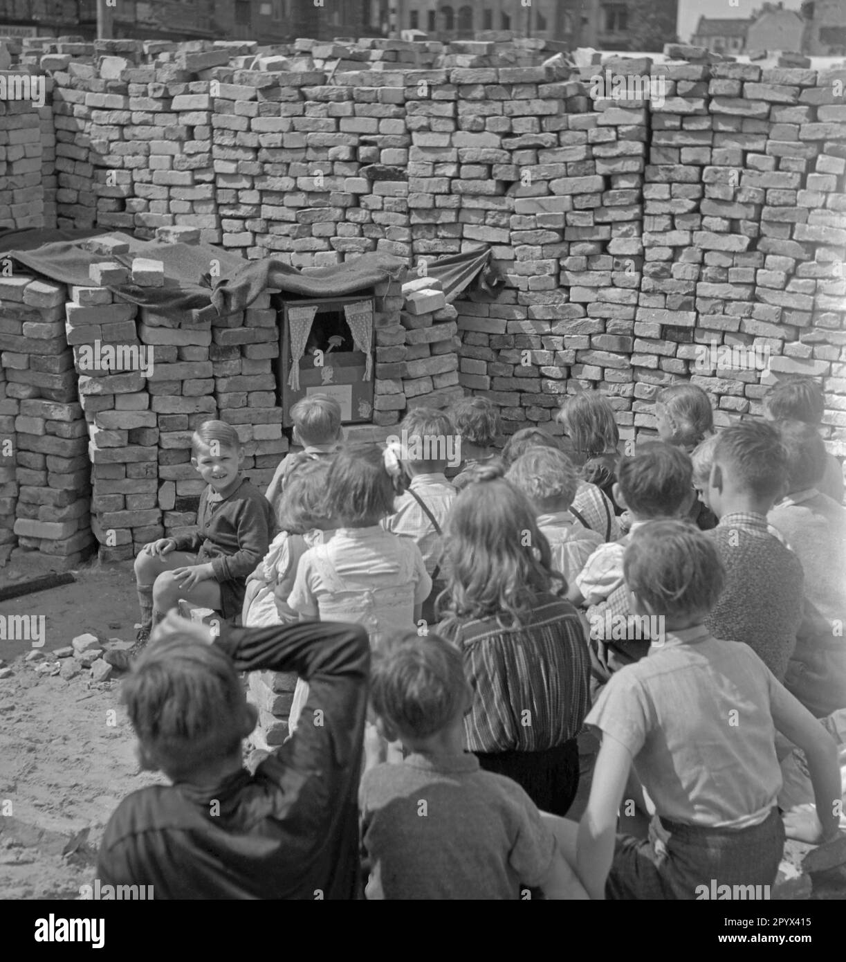 Foto non datata di un gruppo di bambini che guarda uno spettacolo di marionette tra mucchi di mattoni rimanenti dalle rovine. I mattoni servono come tenda per il teatro delle marionette. Foto Stock