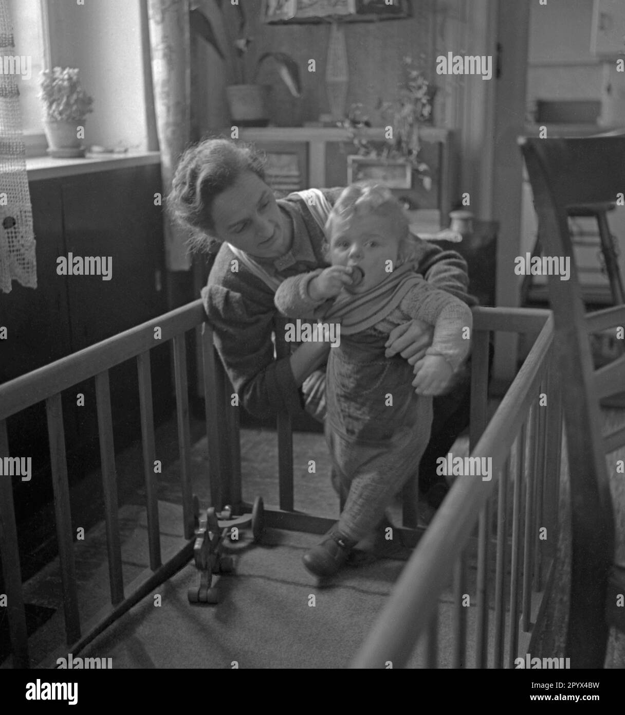 Foto non datata di una nonna che gioca con il nipote in un box in un appartamento, probabilmente a Berlino Ovest, 1950. Essendo un figlio di un soldato tedesco ucciso nella seconda guerra mondiale, il bambino è mezzo-orfano. Foto Stock