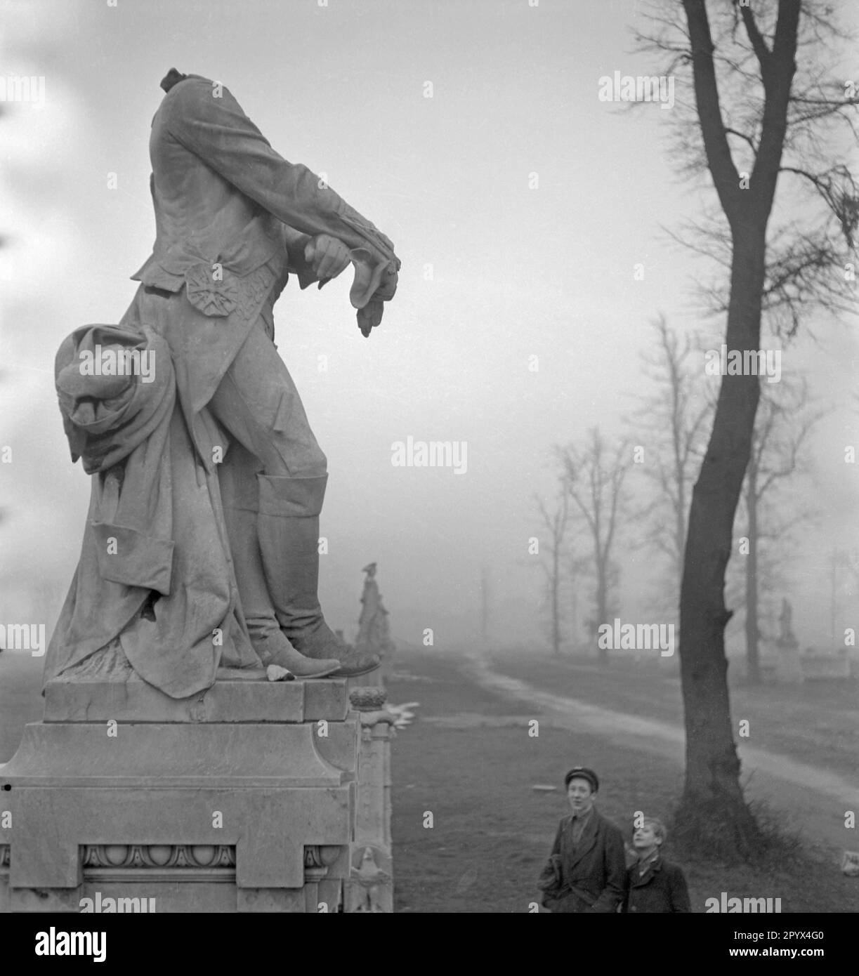 Foto non datata della statua neocarocca in marmo del re Federico Guglielmo II di Prussia (il grasso Luederjahn, 1744-1797, artista Adolf Bruett), parzialmente distrutta dal bombardamento e dal vandalismo dei soldati sovietici (testa mancante), nella Grosse Sternallee nel Tiergarten di Berlino. La statua è presentata con una vista (nord-ovest) della statua luccicante del re Federico Guglielmo III (1770-1840, scultore Gustav Eberlein) nella nebbia e nella colonna della Vittoria alla Grande Stella a Berlino Ovest, un'ex zona di occupazione britannica, 1950. Davanti alla statua, due ragazzi che la guardano. Foto Stock