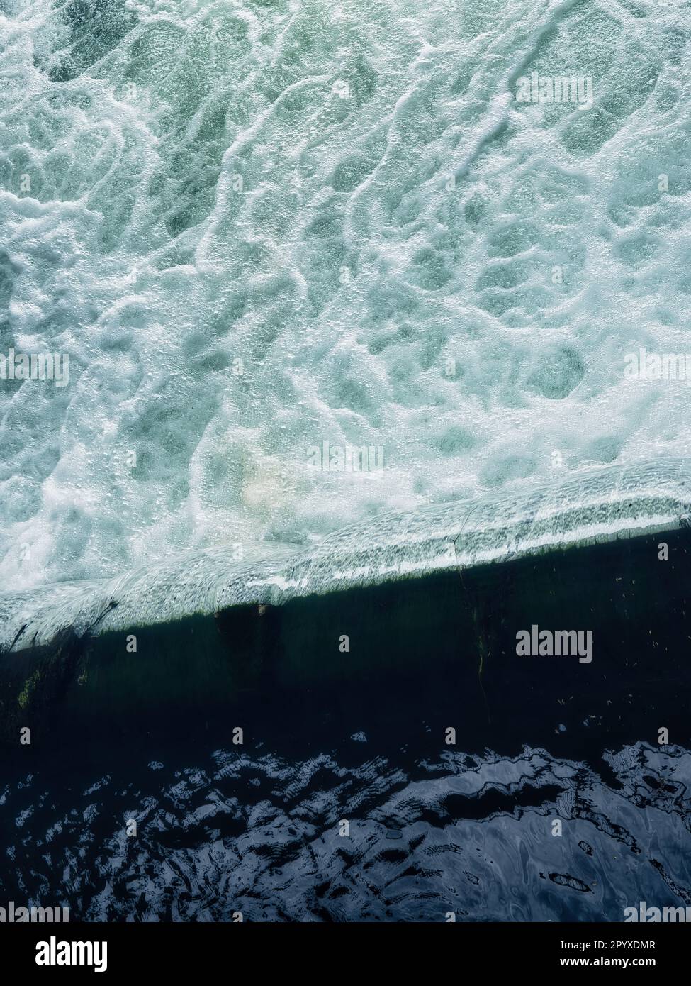 Vista astratta dell'acqua turchese schiumosa che incontra la superficie del mare scuro, mostrando la consistenza delle onde, i motivi naturali e lo sfondo dinamico dell'oceano. Foto Stock