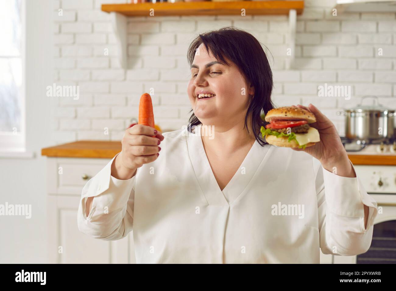 Donna sovrappeso sceglie tra carota e hamburger e decide a favore di un cibo sano Foto Stock