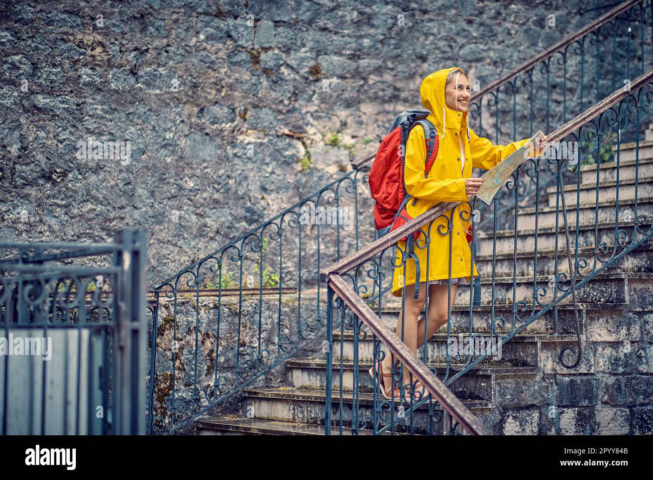 Viaggiare in estate. Giovane donna allegra con mappa, in impermeabile, felice in vacanza. Zaino, turismo, concetto di stile di vita. Foto Stock