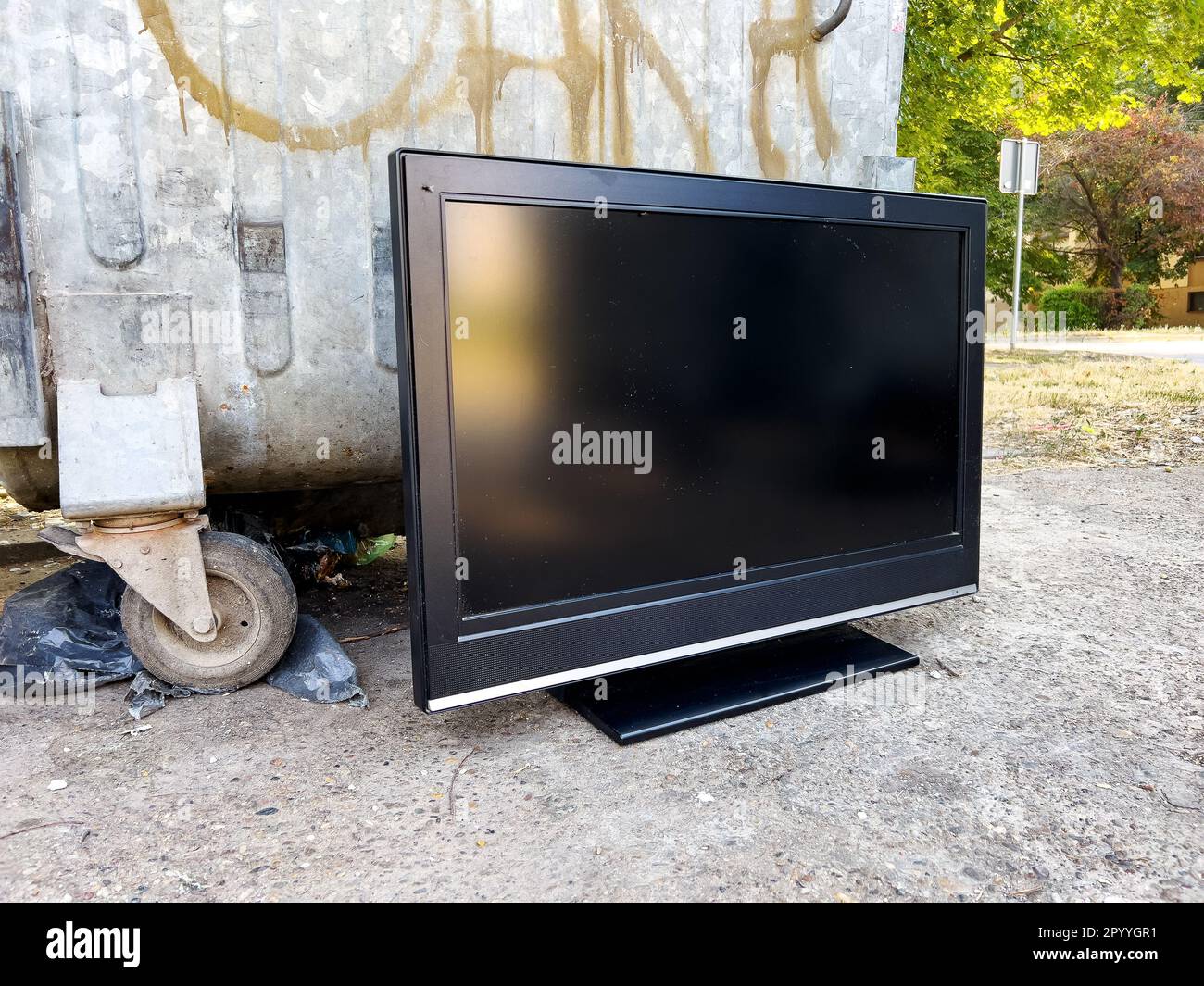 Un vecchio dispositivo tv obsoleto vicino al contenitore dei rifiuti Foto Stock