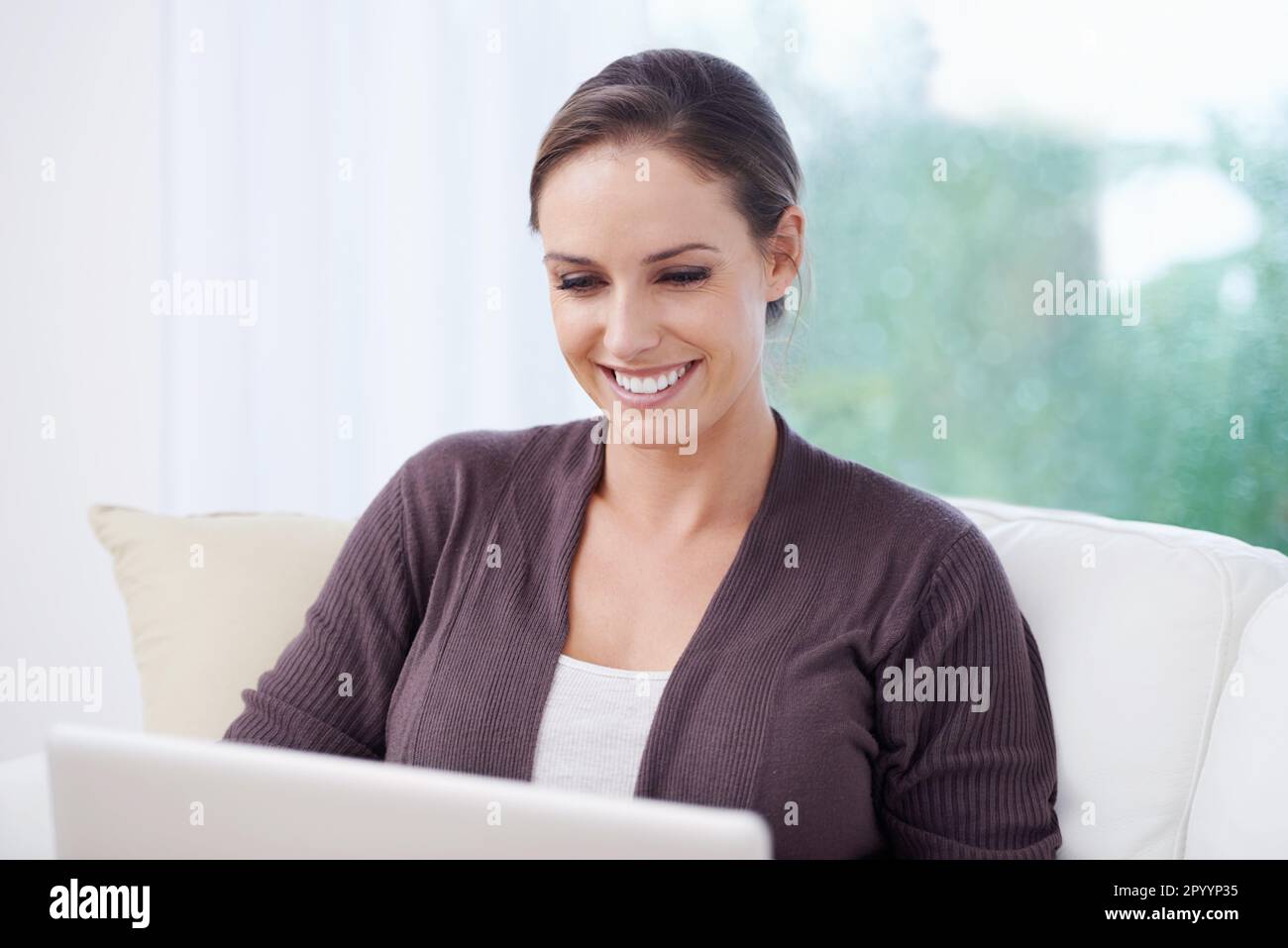 E-mail la mattina presto. Una giovane donna seduta su un divano che lavora sul suo laptop. Foto Stock