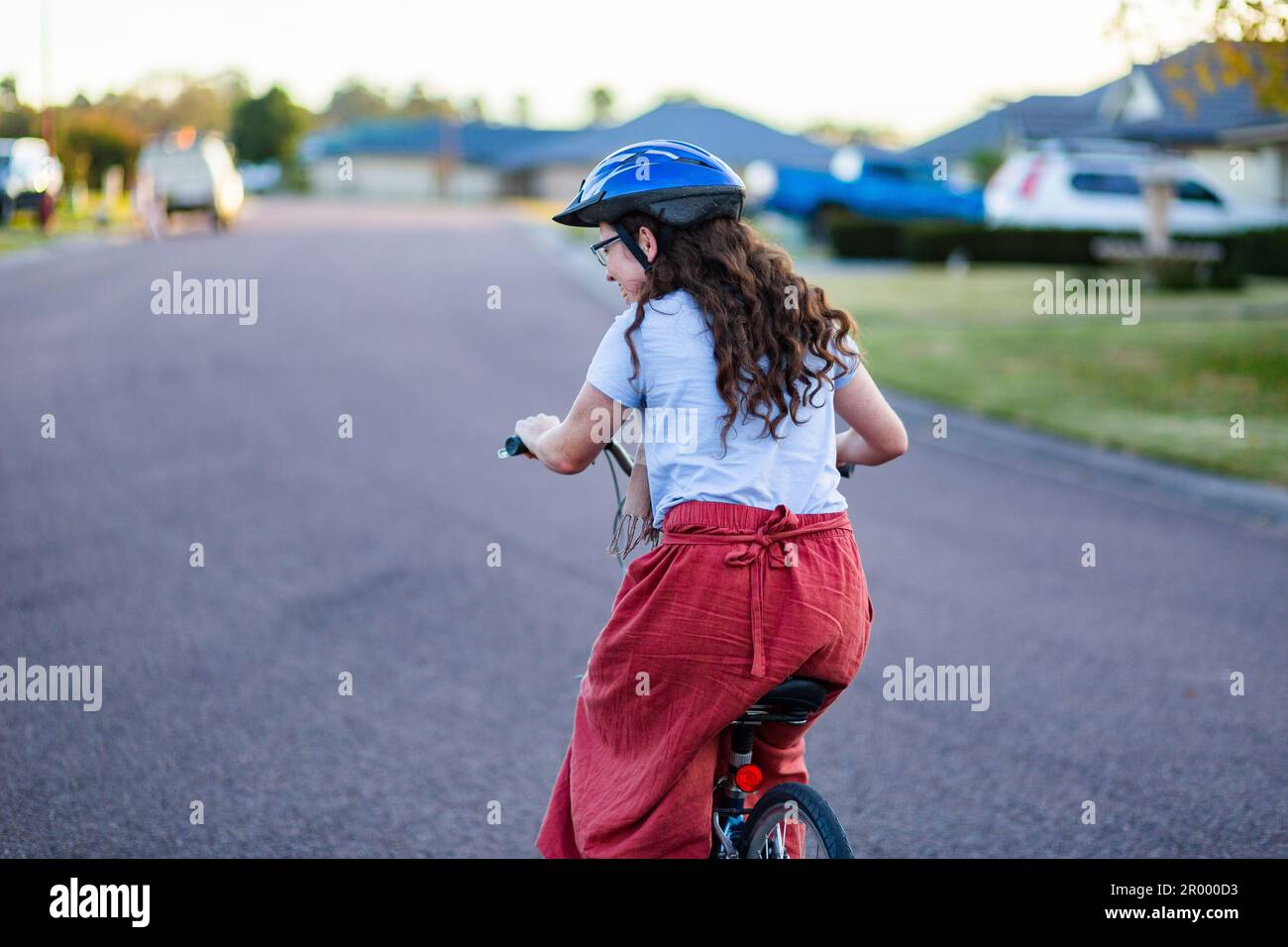 Giovane donna ventenne in sella a una bici su strada suburbana con casco da ciclismo Foto Stock