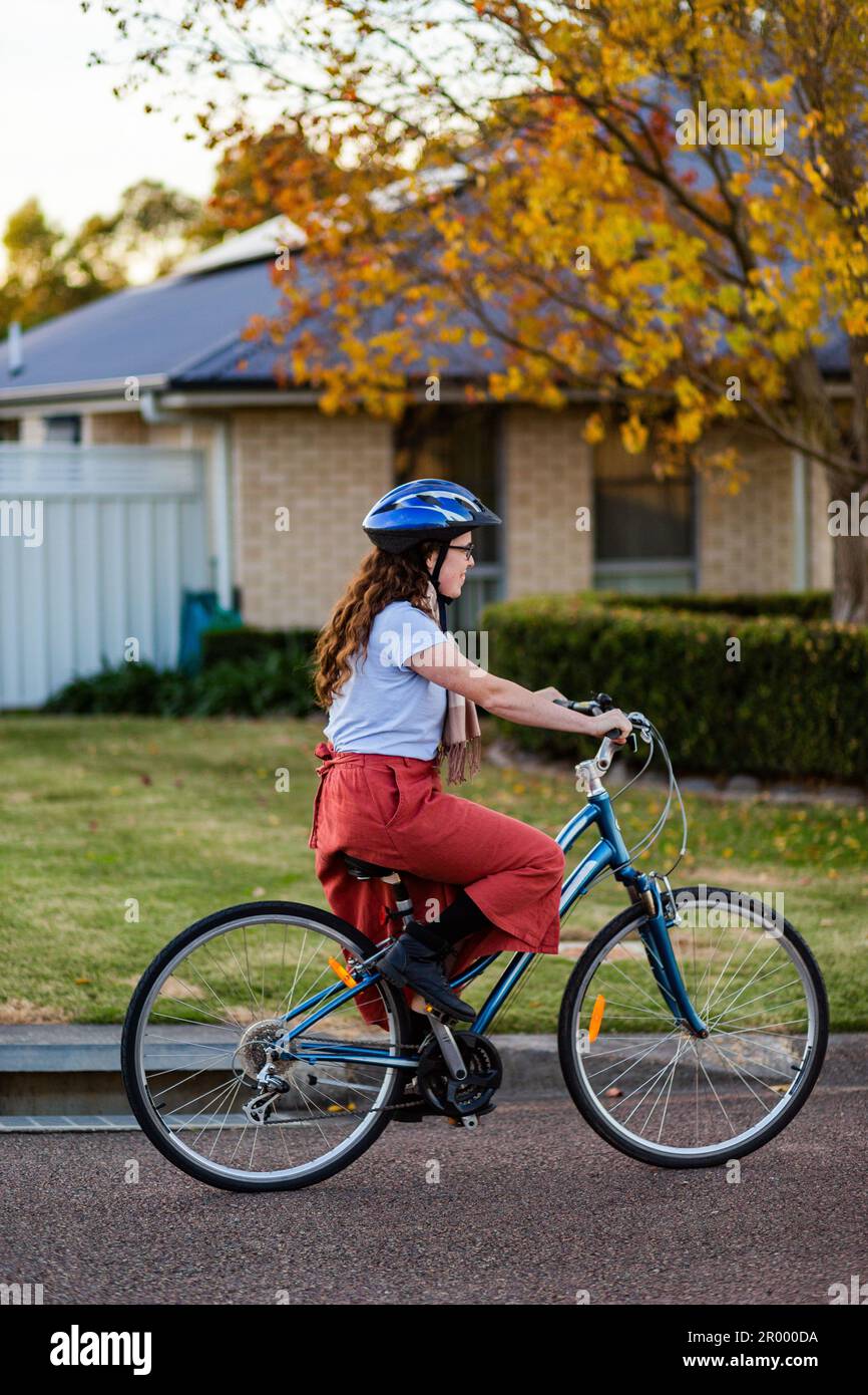 Giovane donna ventenne in sella a una bici su strada suburbana con casco da ciclismo Foto Stock