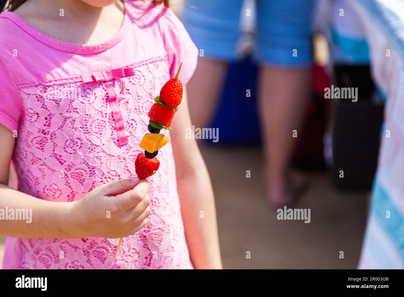 bambina che mangia frutta su un kebab a bastone al mare Foto Stock