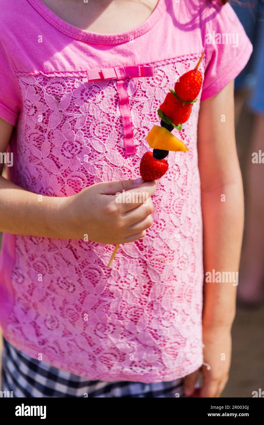 bambina che mangia frutta su un kebab a bastone al mare Foto Stock