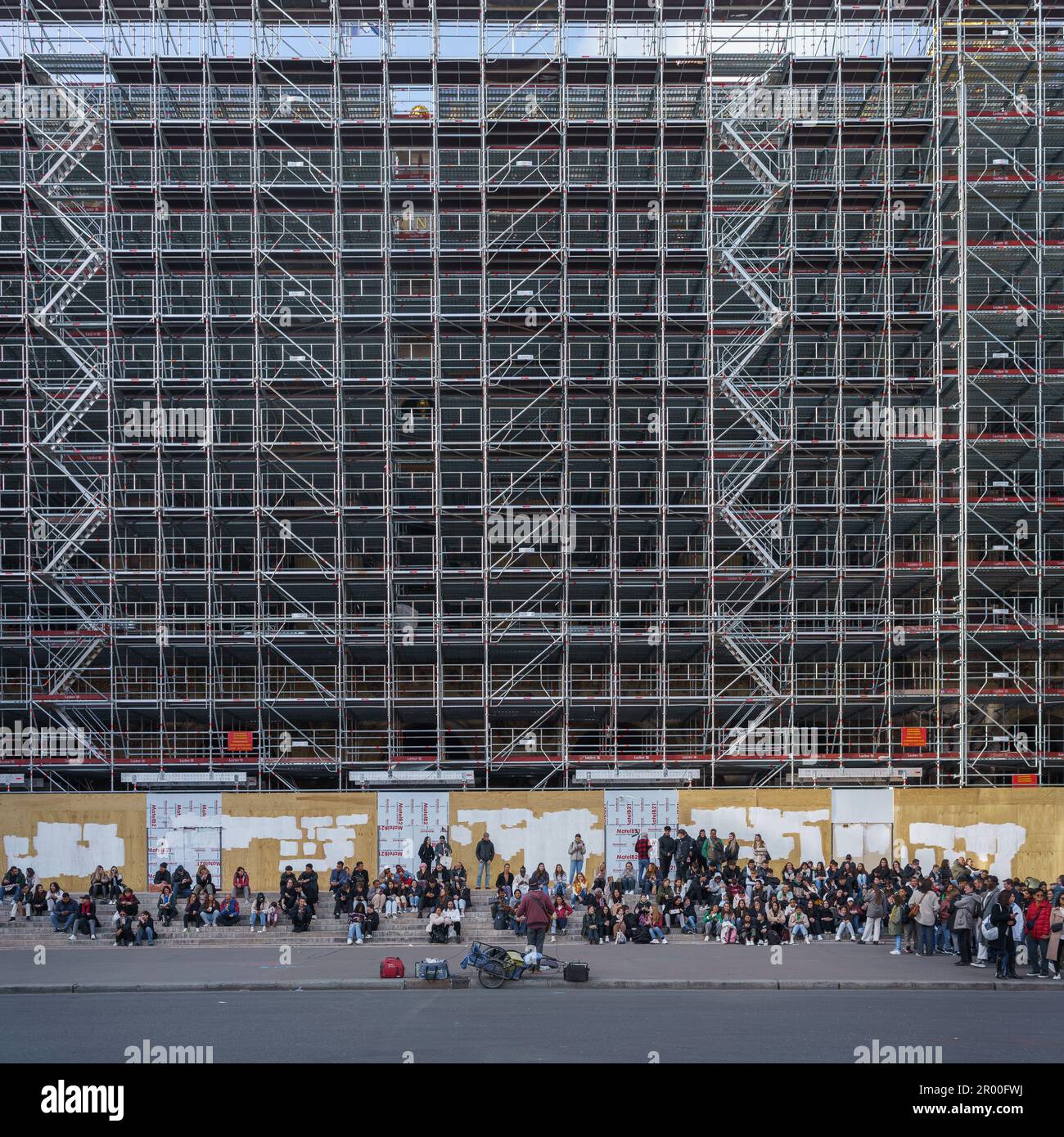 Persone che guardano il musicista di strada di fronte al ponteggio. Ristrutturazione del Palais Garnier a Parigi, Francia. Marzo 25, 2023. Foto Stock