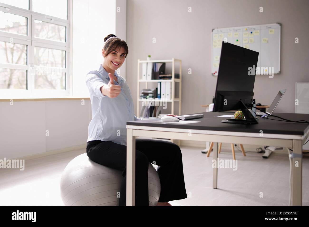 Donna seduta sulla palla palestra in ufficio. Postura corretta Foto Stock